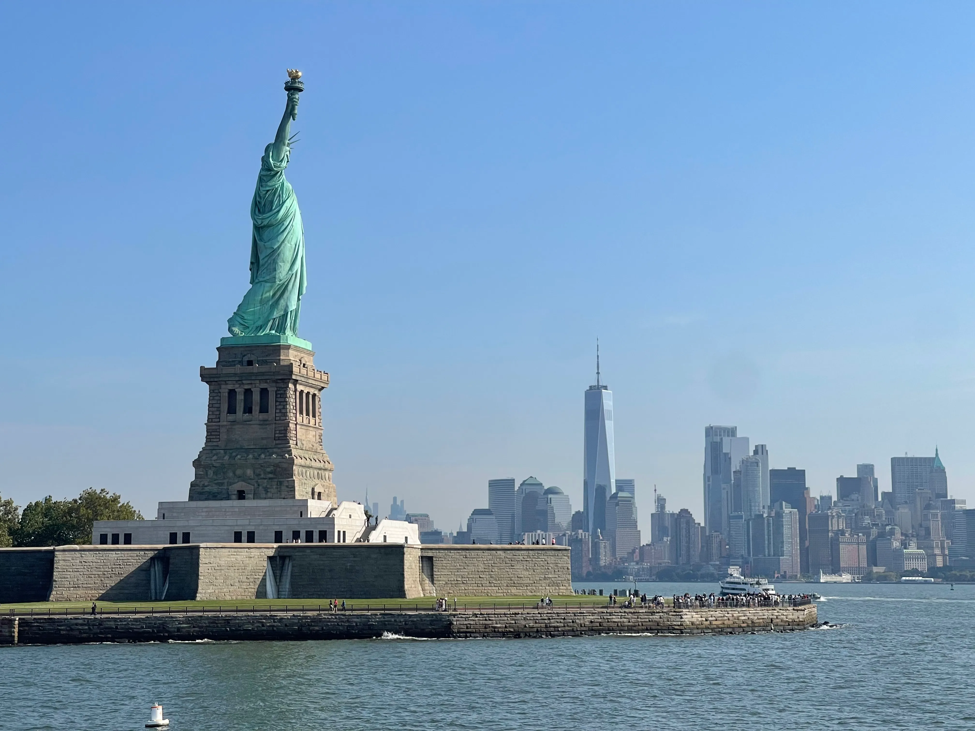 The Statue of Liberty on Liberty Island, with the Lower Manhattan skyline and One World Trade Center across the water behind her