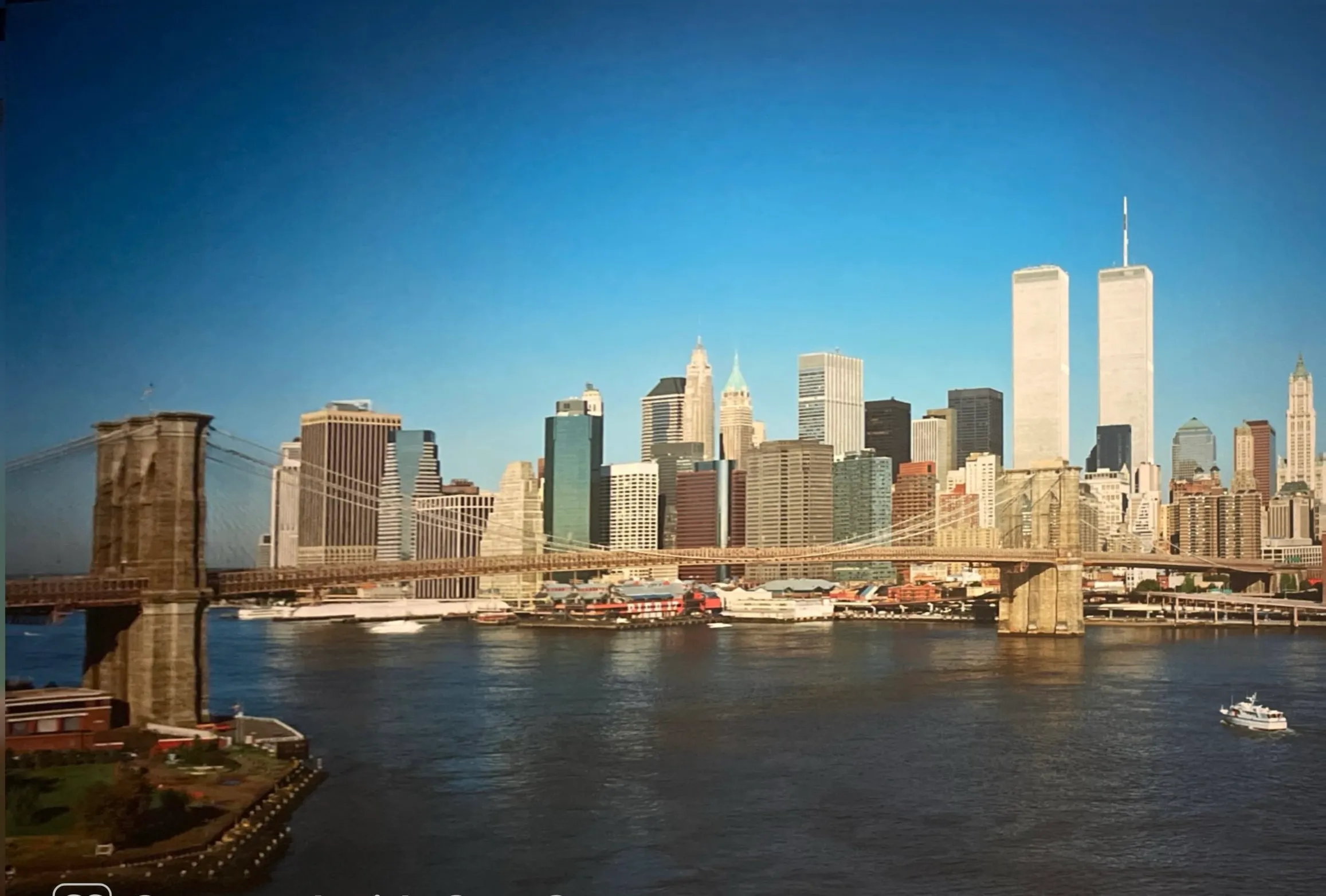 The Lower Manhattan skyline with the Twin Towers standing intact on a clear morning, the Brooklyn Bridge spanning the East River in the foreground